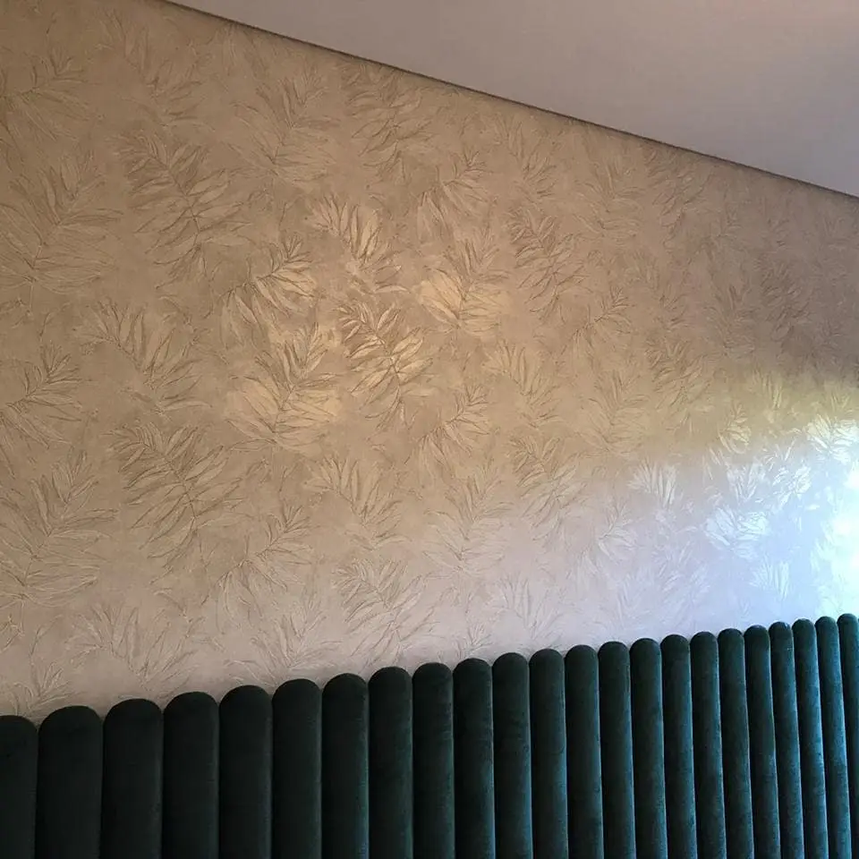 Parede com papel de parede de folhas e cabeceira em veludo verde